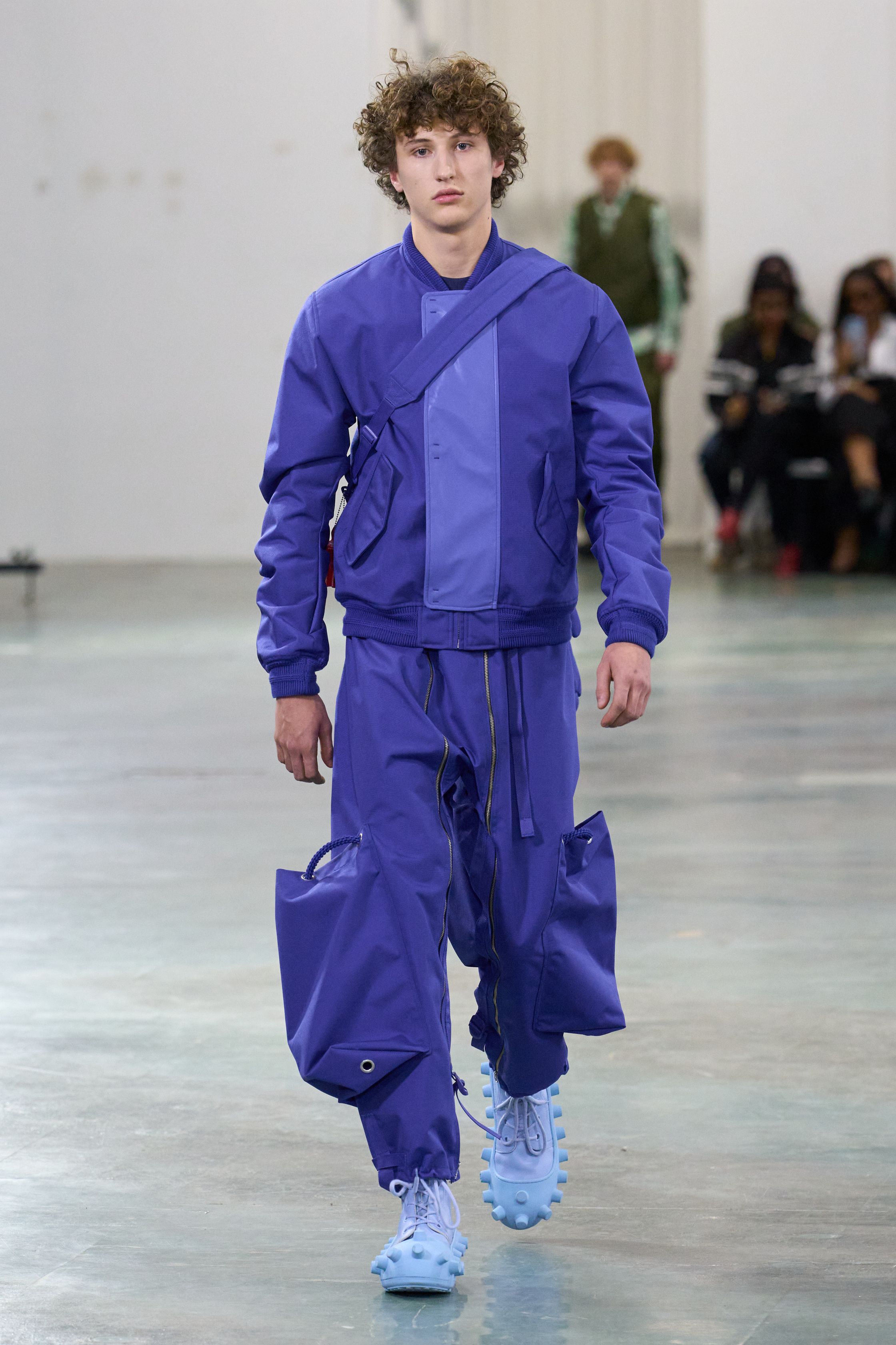 Walter Van Beirendonck 2026秋冬以高度饱和的色彩、夸张比例与童真符号继续挑战男性气质的既定边界。针织花朵、卡通图案、结构化西装与机能裤装并置，构建出介于游戏、政治隐喻与乌托邦幻想之间的舞台。系列拒绝低调，刻意制造视觉噪音，用快乐、怪诞与不合时宜的色彩作为对现实焦虑的反击，呈现一场毫不妥协的时装宣言-顽石频道趋势研究